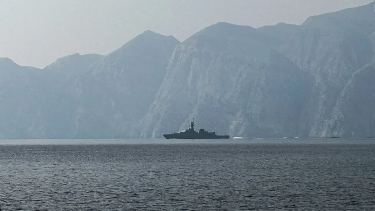 A navy vessel navigates the Strait of Hormuz, a critical oil conduit, as market attention centers on U.S.–Iran negotiations.